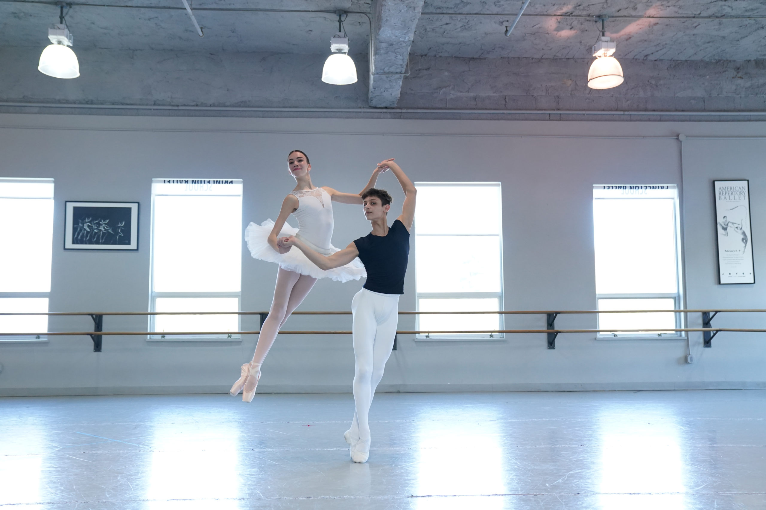 Two dancers in studio, one lifting the other.