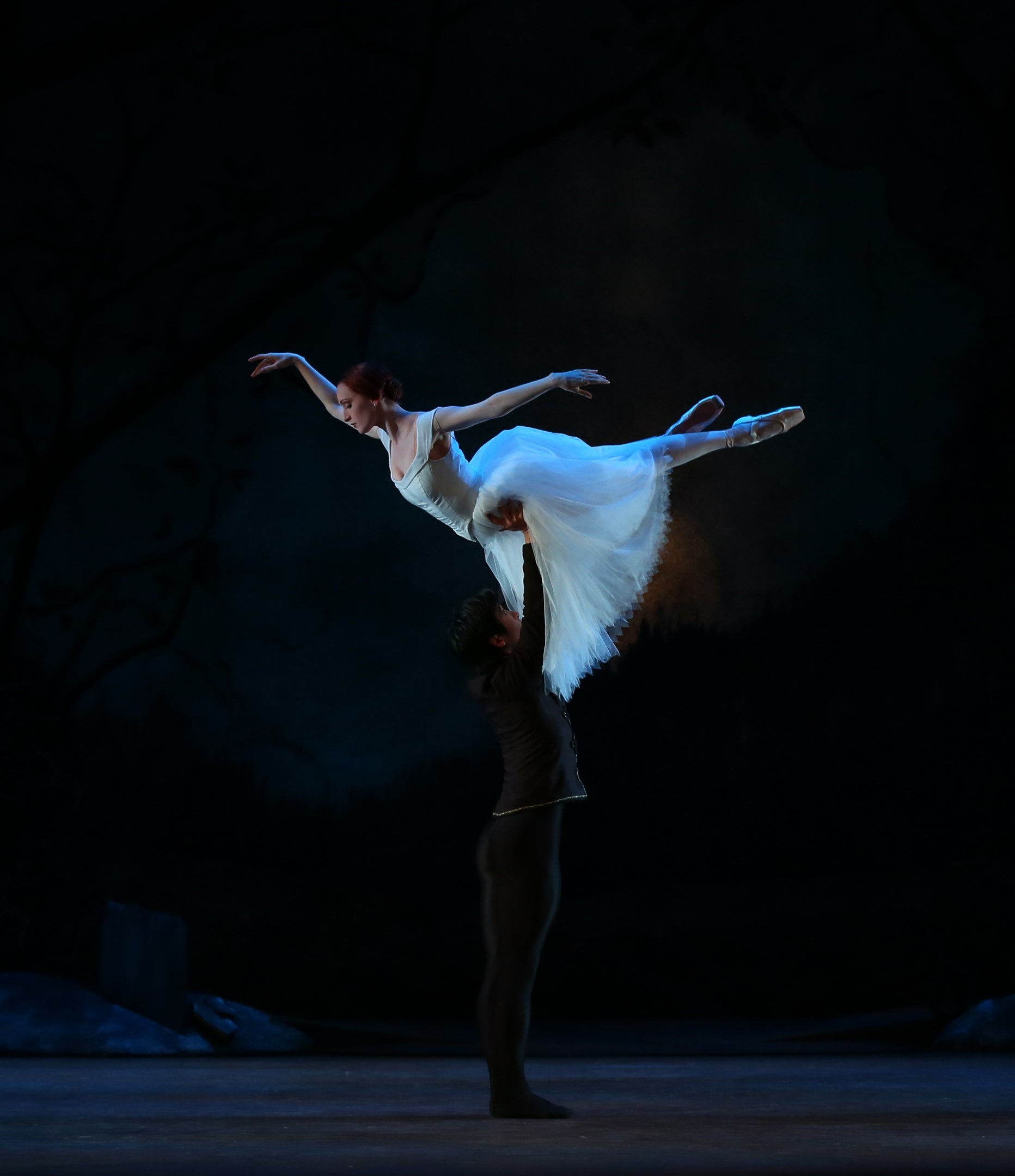 Dancer in white dress being lifted with dramatic lighting.